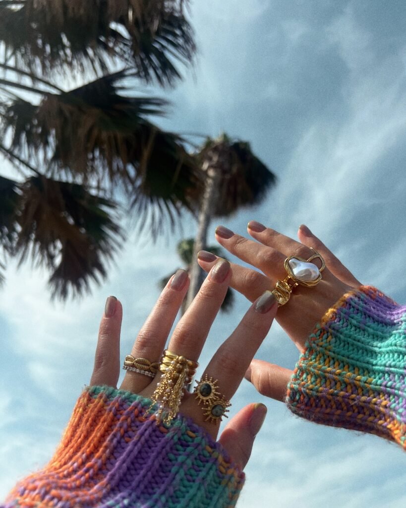 Colorful sweater and gold rings against palm tree and sky background. Vibrant fashion accessories.