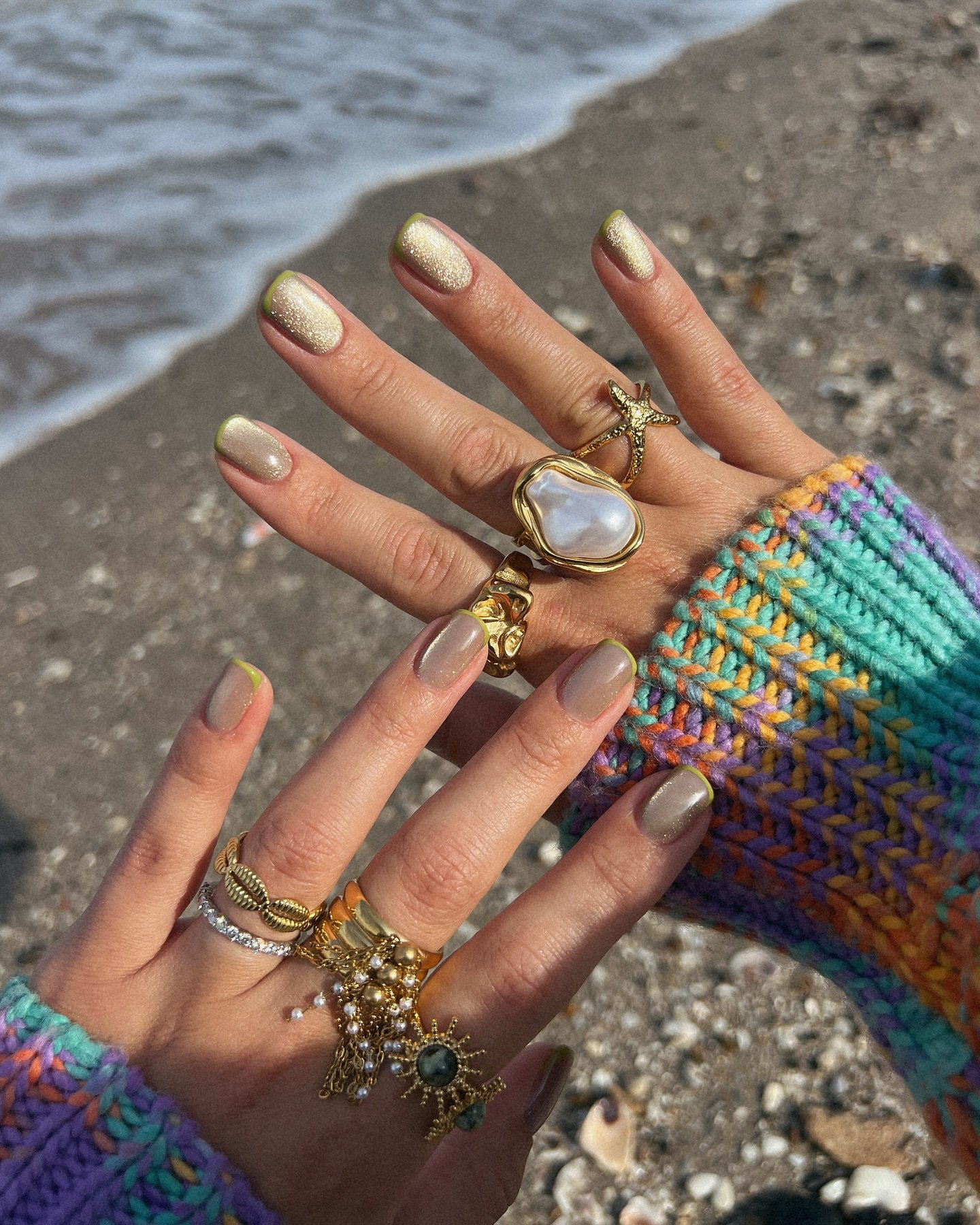 Colorful nails and gold rings on the beach, showcasing vibrant fashion and accessories.