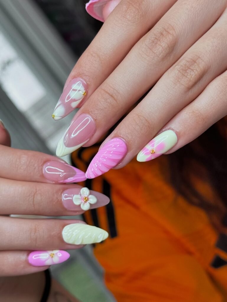 Colorful spring-themed nail art with floral accents and pink, white, and green designs on manicured hands.