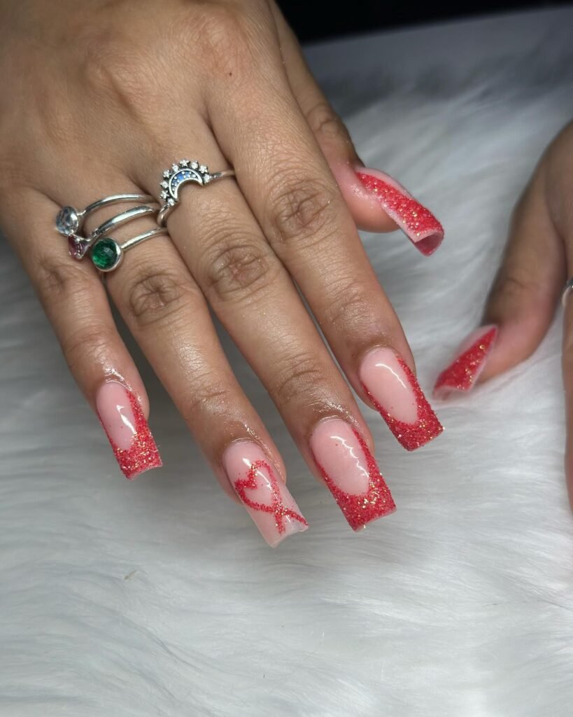 Red glitter heart nail art with square tips on manicured hand, adorned with silver rings, over a white fur background.