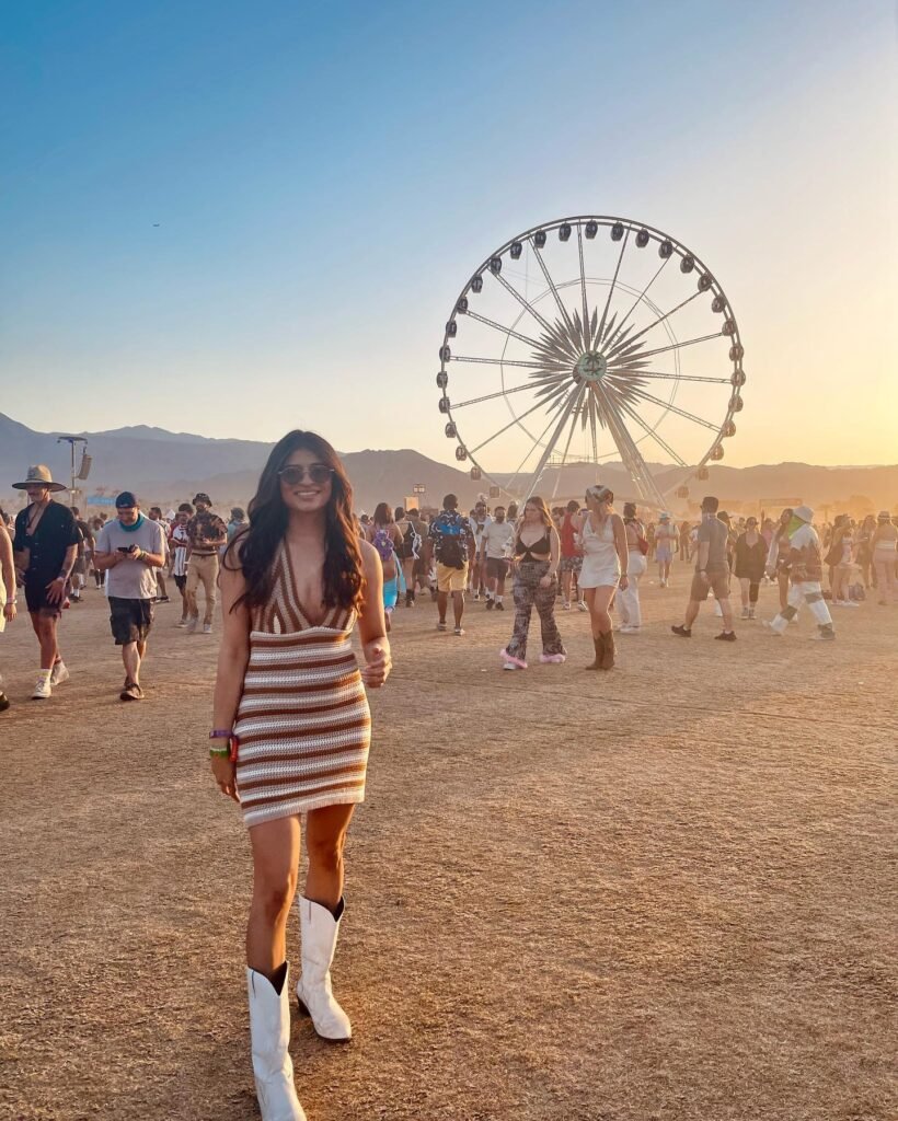 Festival-goer in dress and boots at sunset with Ferris wheel in background.