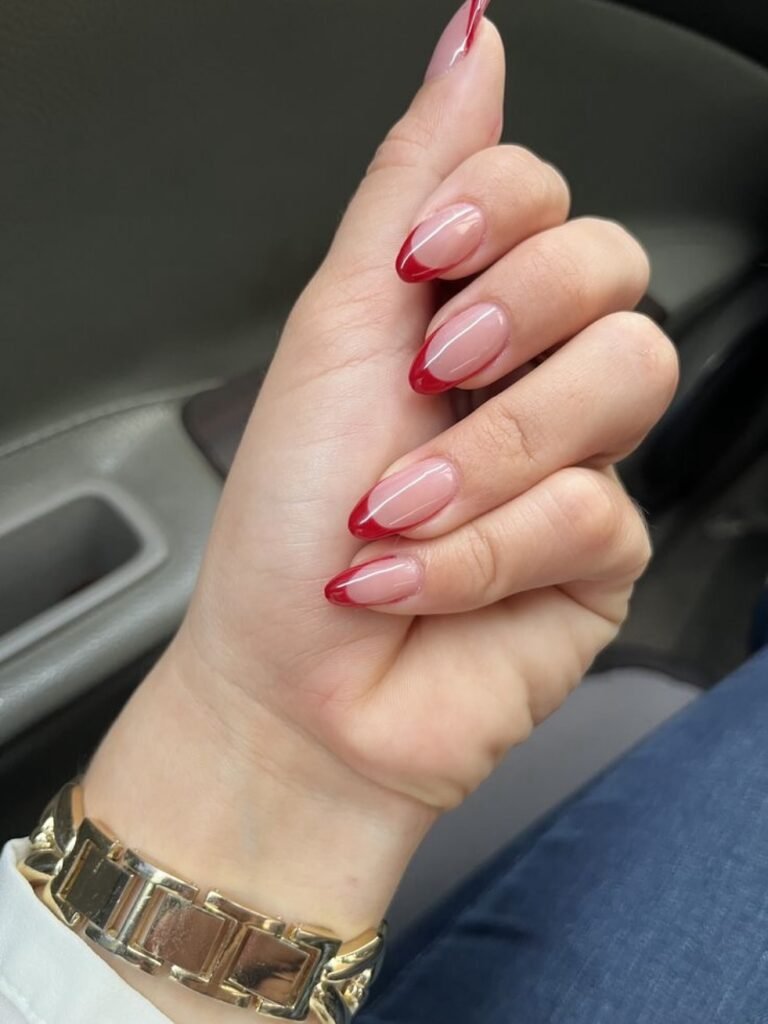 Stylish nails with red French tips and gold watch, showcasing elegant nail art and fashion accessory.