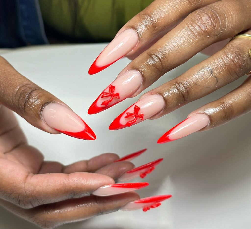 Stiletto nails with red French tips and bow designs, perfect for a bold and stylish manicure look.