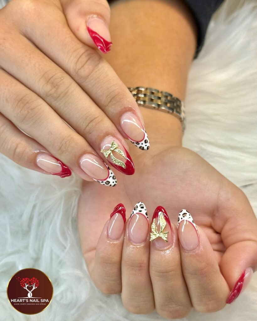 Red and white nail art with gold accents and animal print, held in front of a fluffy background.
