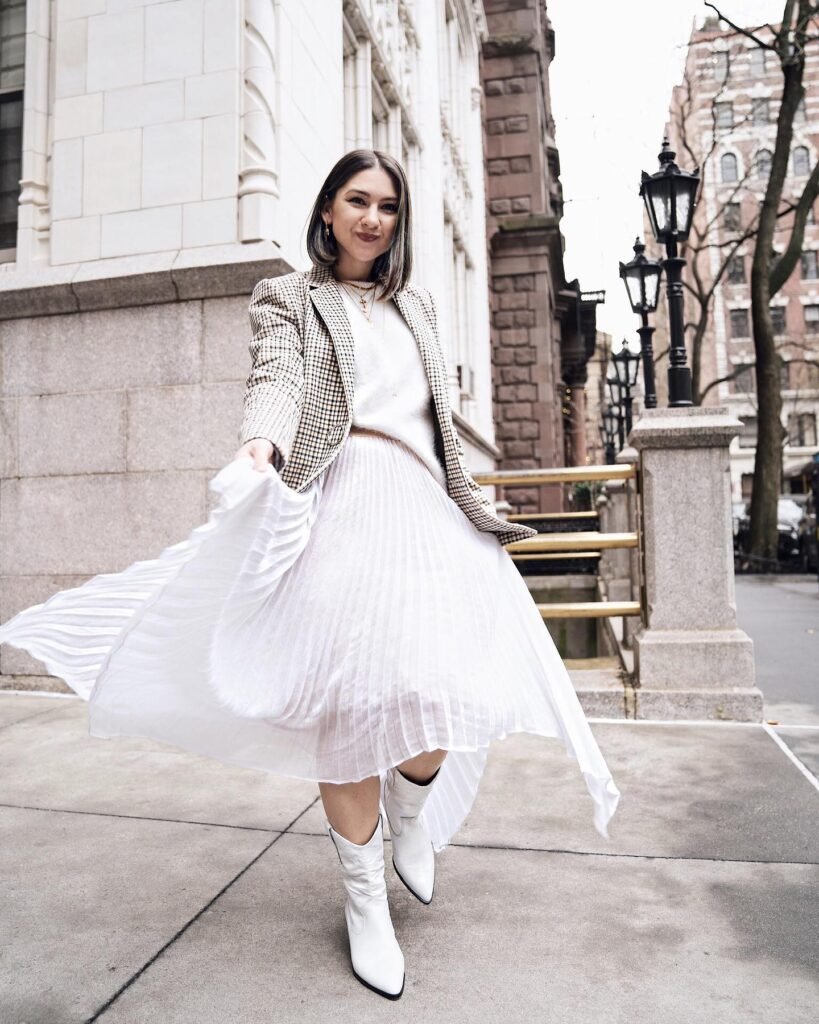 Woman in white pleated dress and blazer, walking in city street, showcasing fashion style.