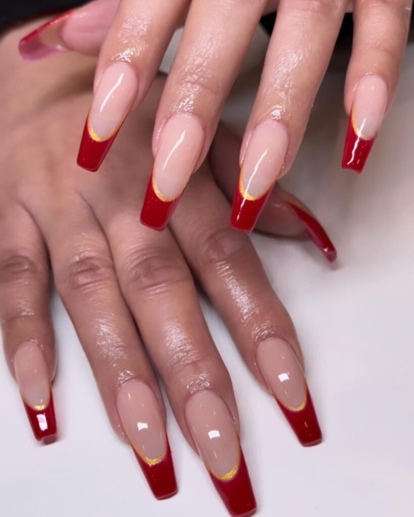 Red and gold French tip nails with a glossy finish; stylish manicure on long coffin-shaped nails.