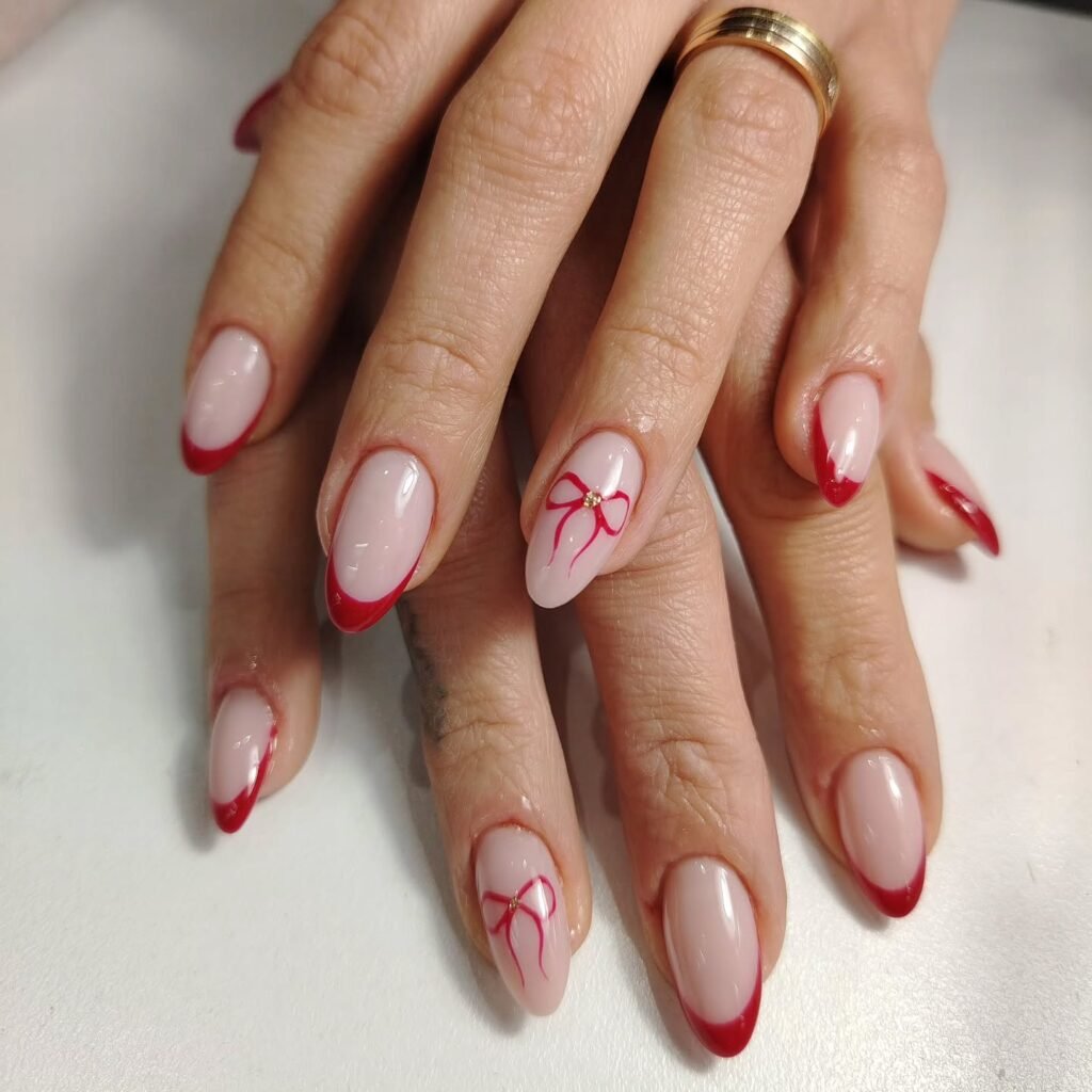 Red-tipped nails with a bow accent on ring finger, showcasing elegant manicure design.