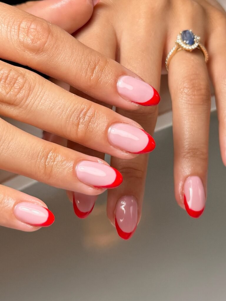 Elegant hands with red French tip nails and a sapphire ring.