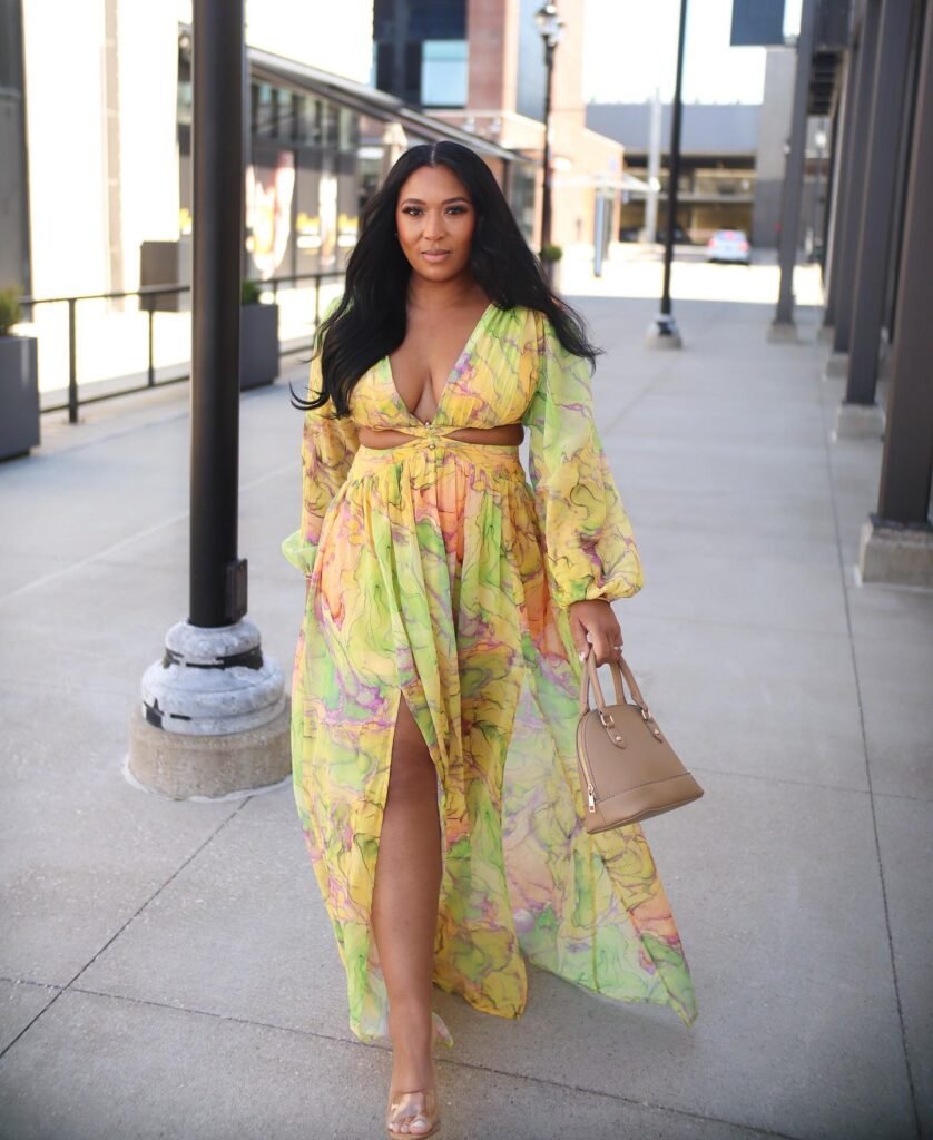 Woman in colorful, flowing dress walking down city sidewalk, carrying a tan handbag.