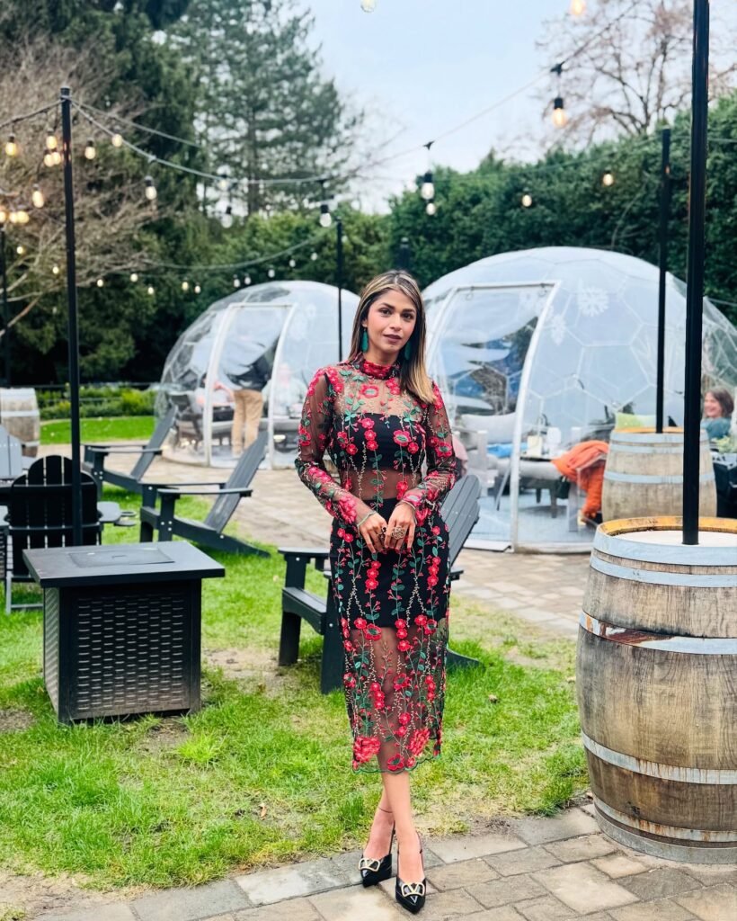Woman in floral dress posing outdoors at a stylish garden venue with string lights and igloo-style seating.