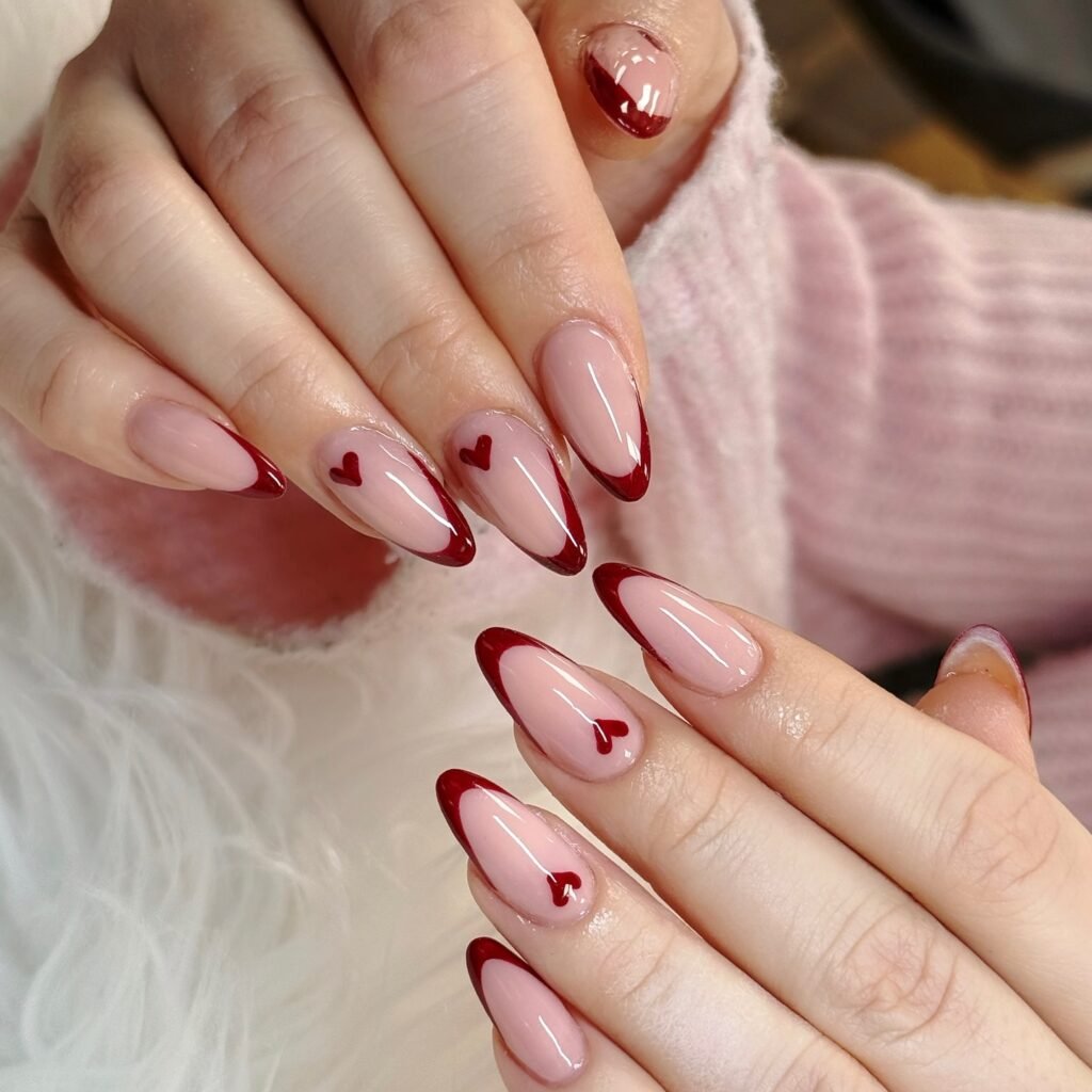 Stylish red and pink French manicure with heart accents on almond-shaped nails.