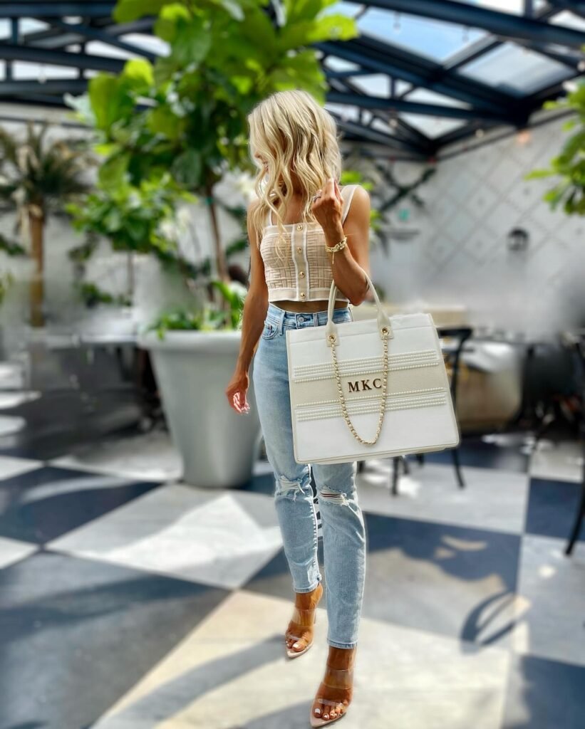 Blonde woman in trendy outfit with oversized handbag in a stylish, sunlit cafe setting.