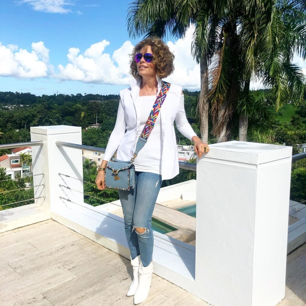 Stylish woman in sunglasses enjoying a sunny terrace with lush palm trees and blue sky in the background.