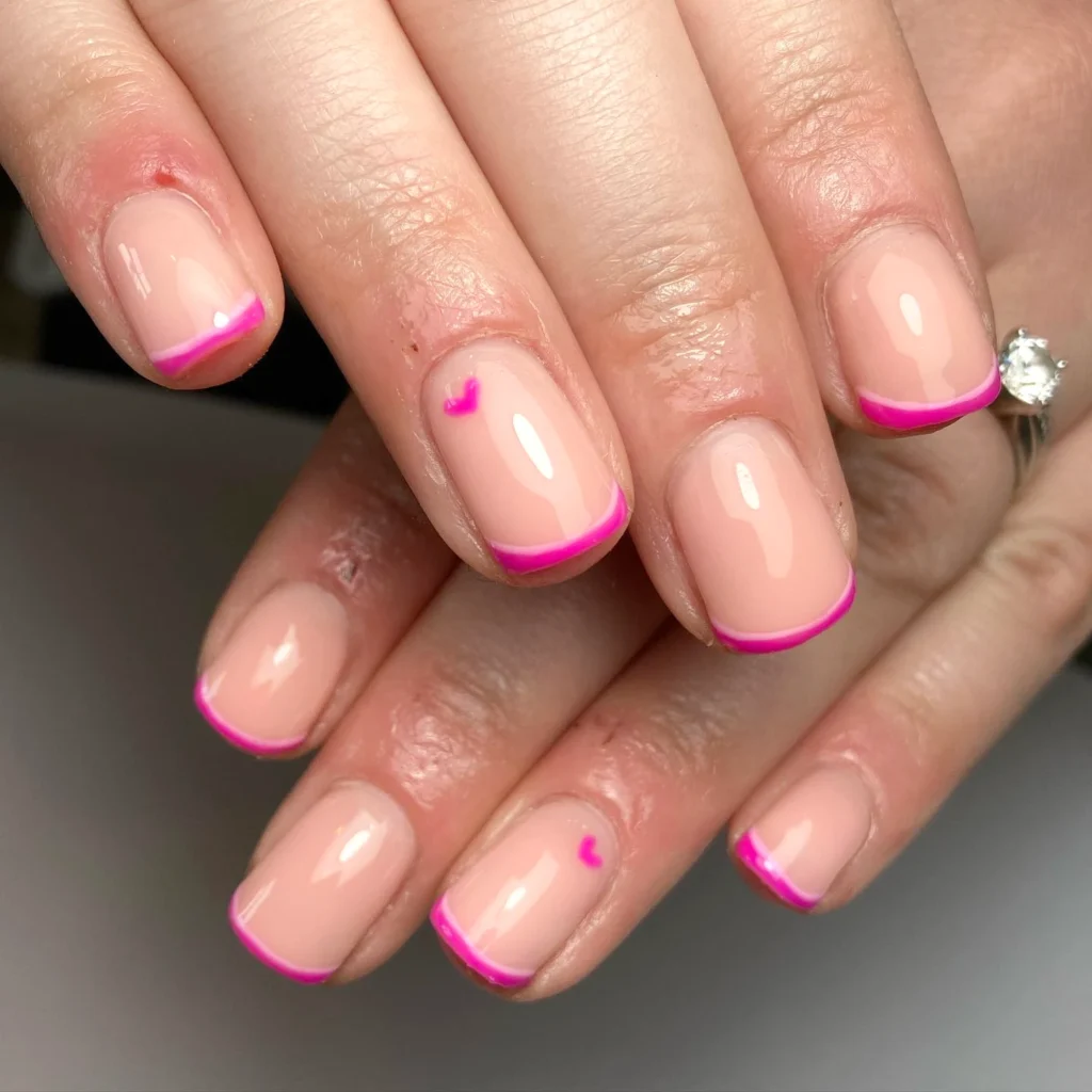 Nude nails with pink French tips and small heart details, showcasing a stylish, modern manicure design.