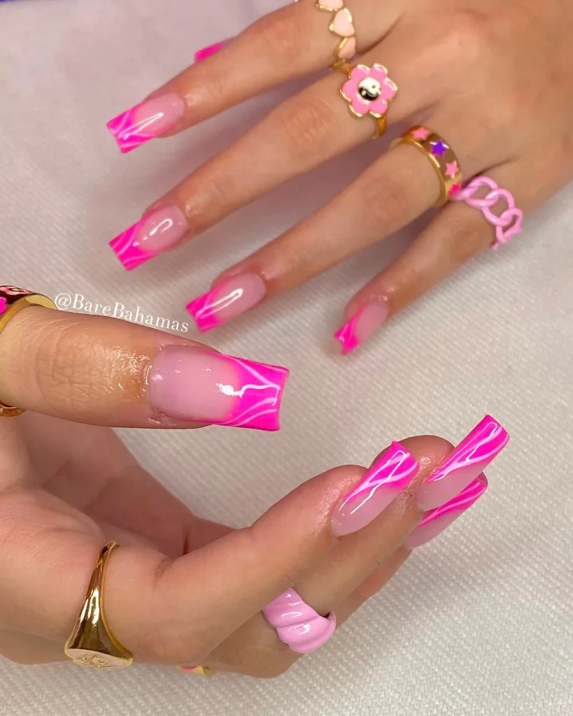 Pink swirl nail art with gold and enamel rings on manicured hands, showcasing trendy nail design and accessories.