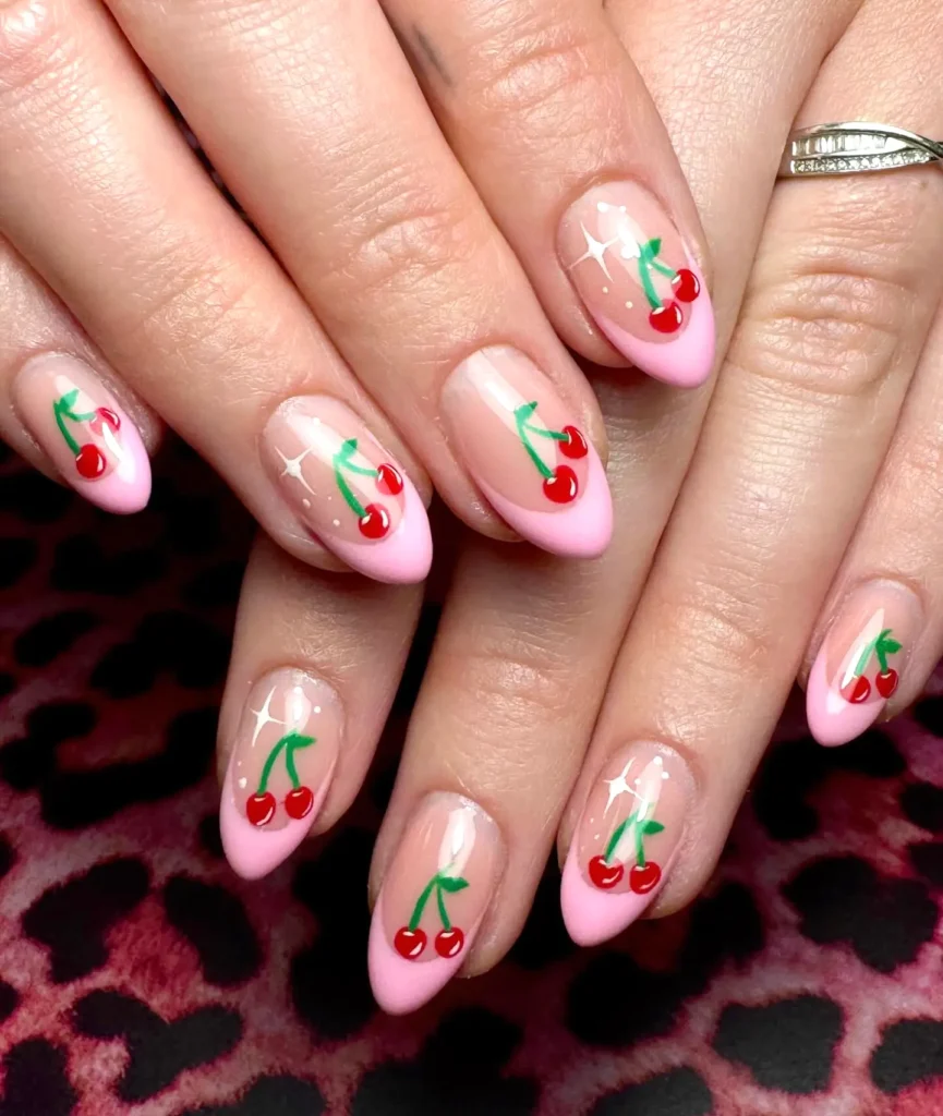 Pink almond nails with cherry nail art design on a leopard print background.