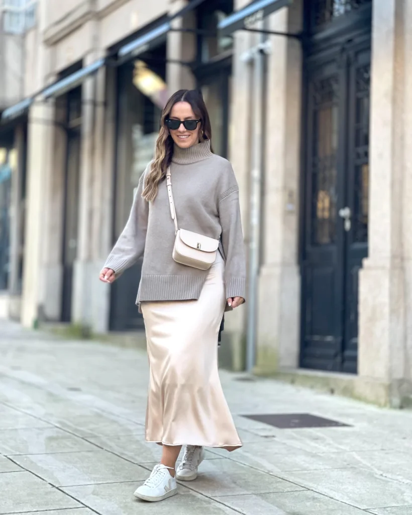 Woman in stylish beige outfit and sunglasses walking on urban street, smiling confidently.