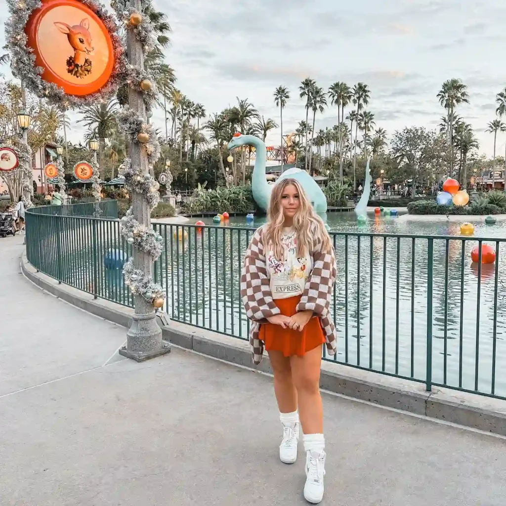 Woman in winter fashion by festive decorations and lake at theme park.