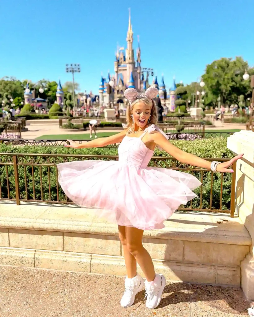 Woman in pink dress and mouse ears at Disney park with castle in background.