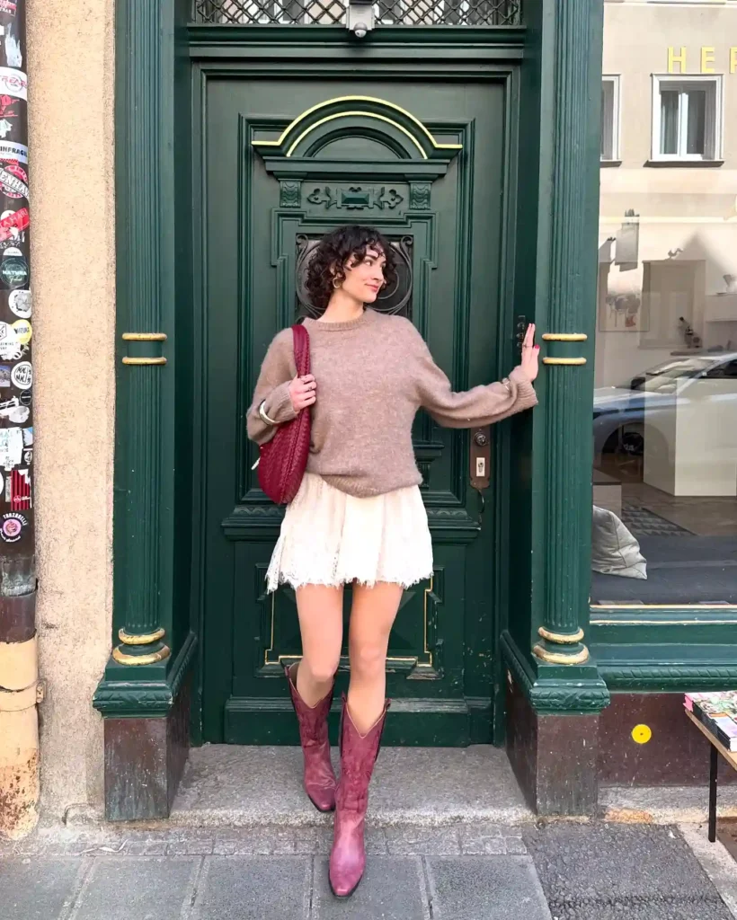 Woman in casual outfit with red boots and bag standing by green decorative door, posed stylishly.