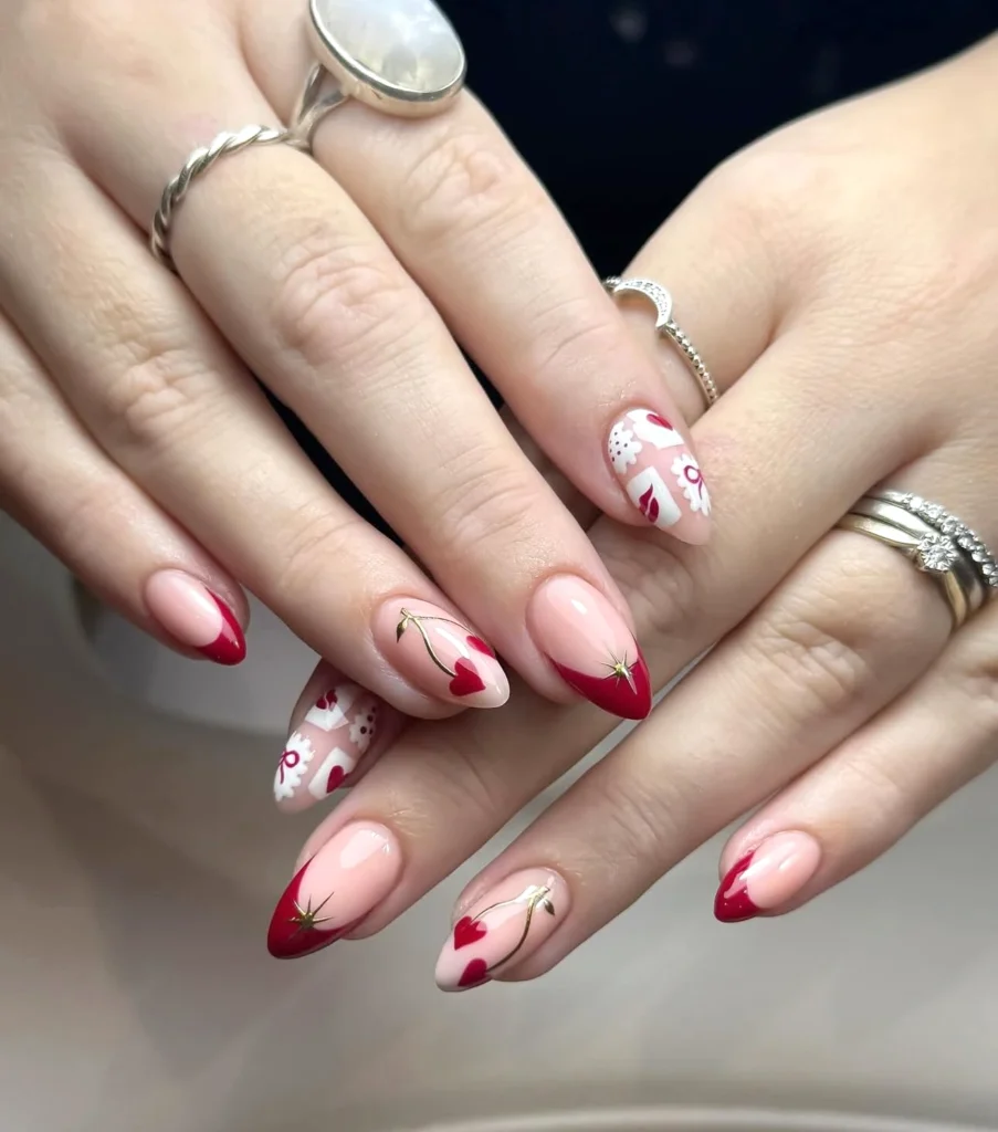 Elegant Valentine's nail art with red tips, hearts, and floral designs on manicured hands wearing silver rings.