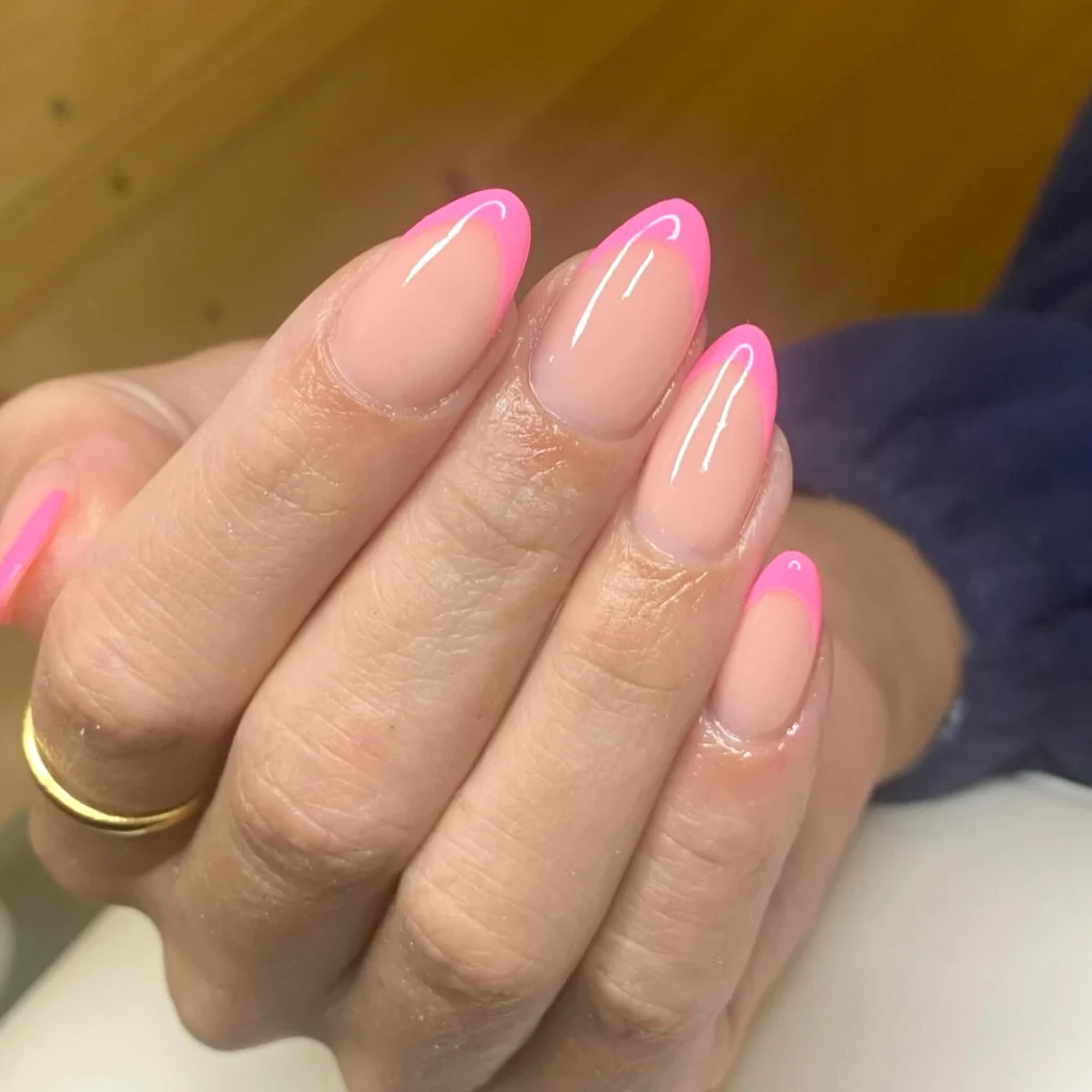 Close-up of a hand showing a pink-tipped nail design on almond-shaped nails. Suitable for nail art inspiration.