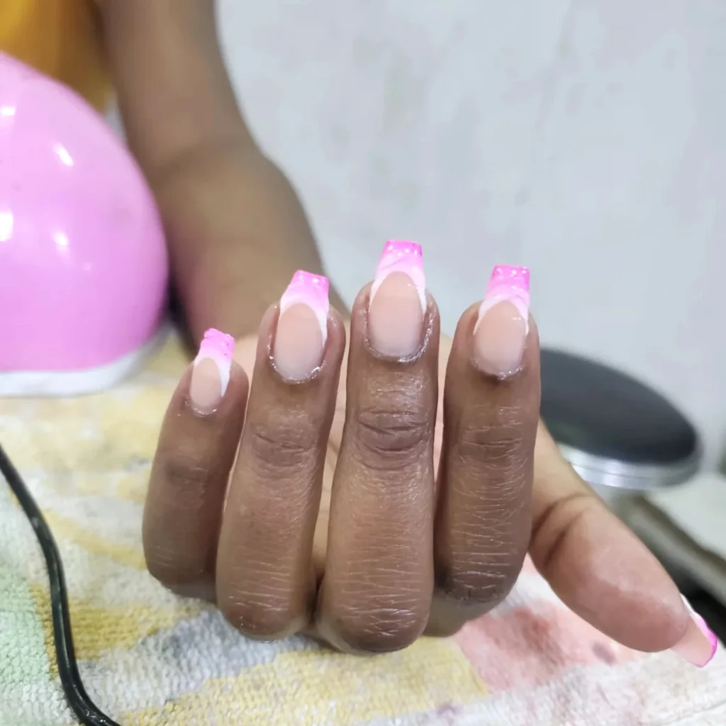 Pink ombre French manicure with gel finish on a hand, resting on a towel near a pink nail lamp.