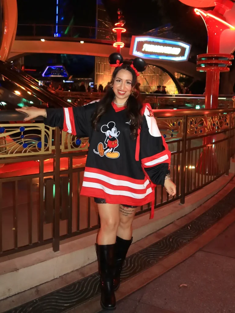 Woman in Mickey Mouse attire enjoys a night at a theme park with colorful lights and decorations.