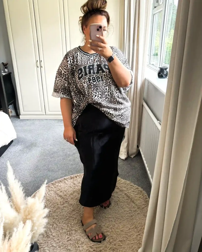 Person wearing a Paris 1984 leopard print shirt and black skirt, taking a selfie in a mirror-lit room.