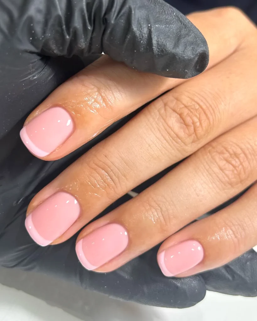 Close-up of a manicured hand with glossy pink nails, held by a gloved hand, showcasing nail art.