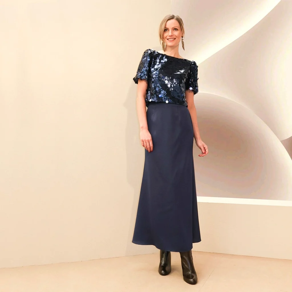 Woman in elegant navy sequin top and long skirt, posing in stylish background ambiance.
