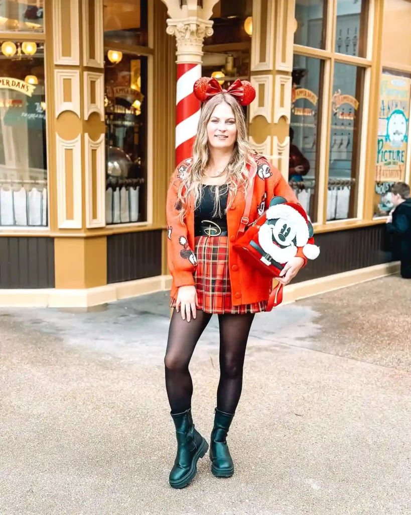 Woman in festive red outfit with Mickey Mouse accessory at theme park entrance.