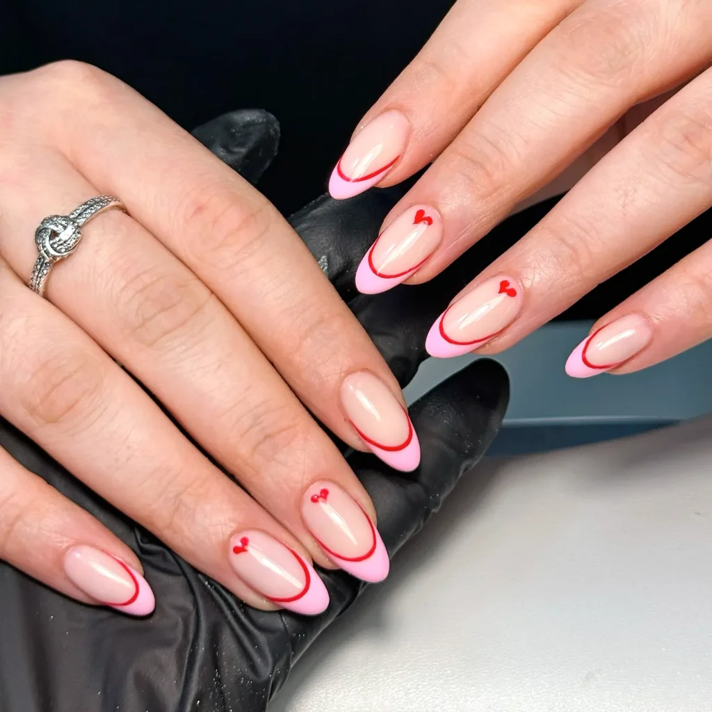 Stylish pink French manicure with red heart accents on almond-shaped nails. Perfect Valentine's Day nail art.