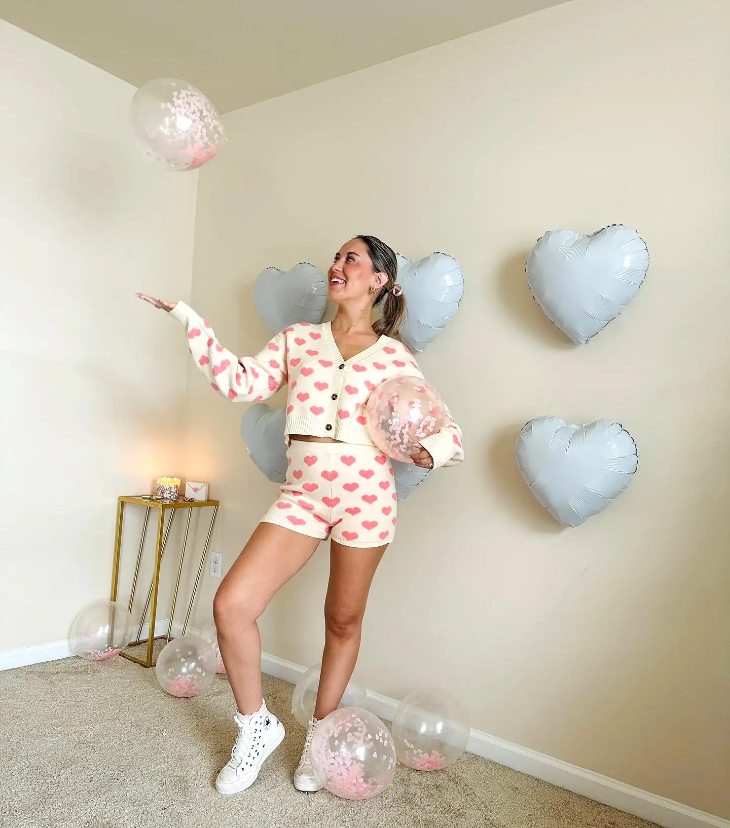 Person in a heart-patterned outfit playfully juggling balloons with heart-shaped decor.