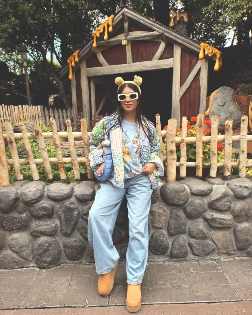 Woman in themed outfit and bear ears poses in front of rustic wooden cottage with playful decor.