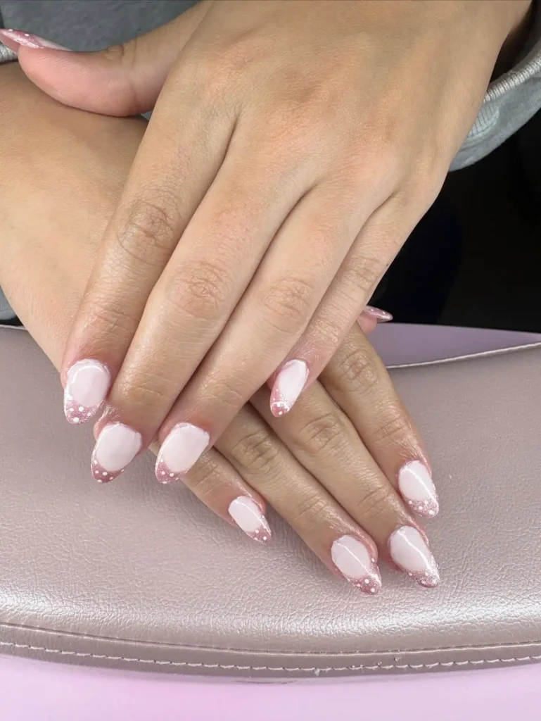 Elegant hands with pink manicure and sparkly tips, resting on a textured surface, showcasing nail art beauty.