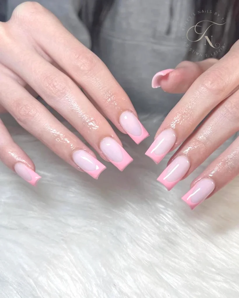 Hands with glossy pink French ombre acrylic nails on a soft surface.