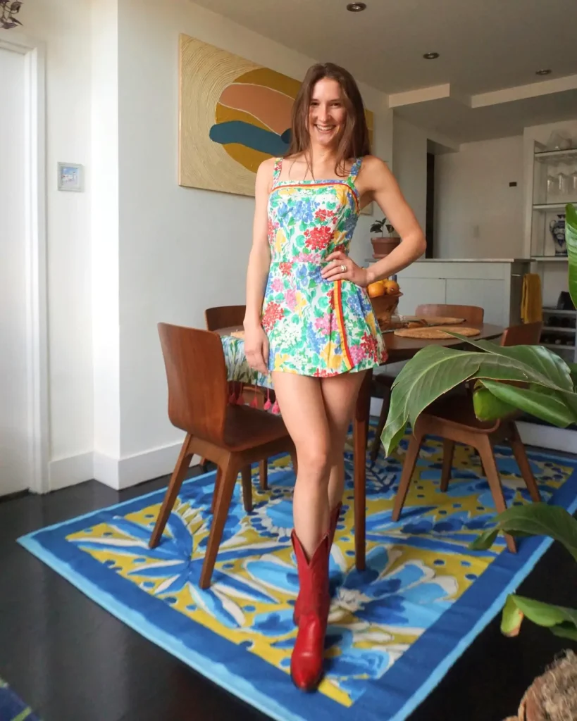 Woman in colorful floral dress and red boots smiling in a modern living room with vibrant decor.