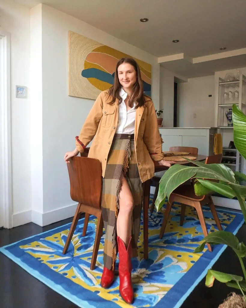 Woman in stylish outfit with red boots poses in modern living room with colorful decor.