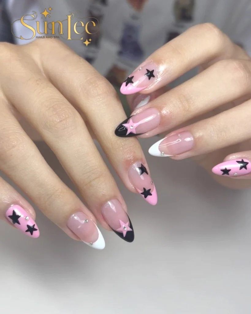 Pink and black star nail art with rhinestones on long almond-shaped nails at Sunlee Nails and Spa.