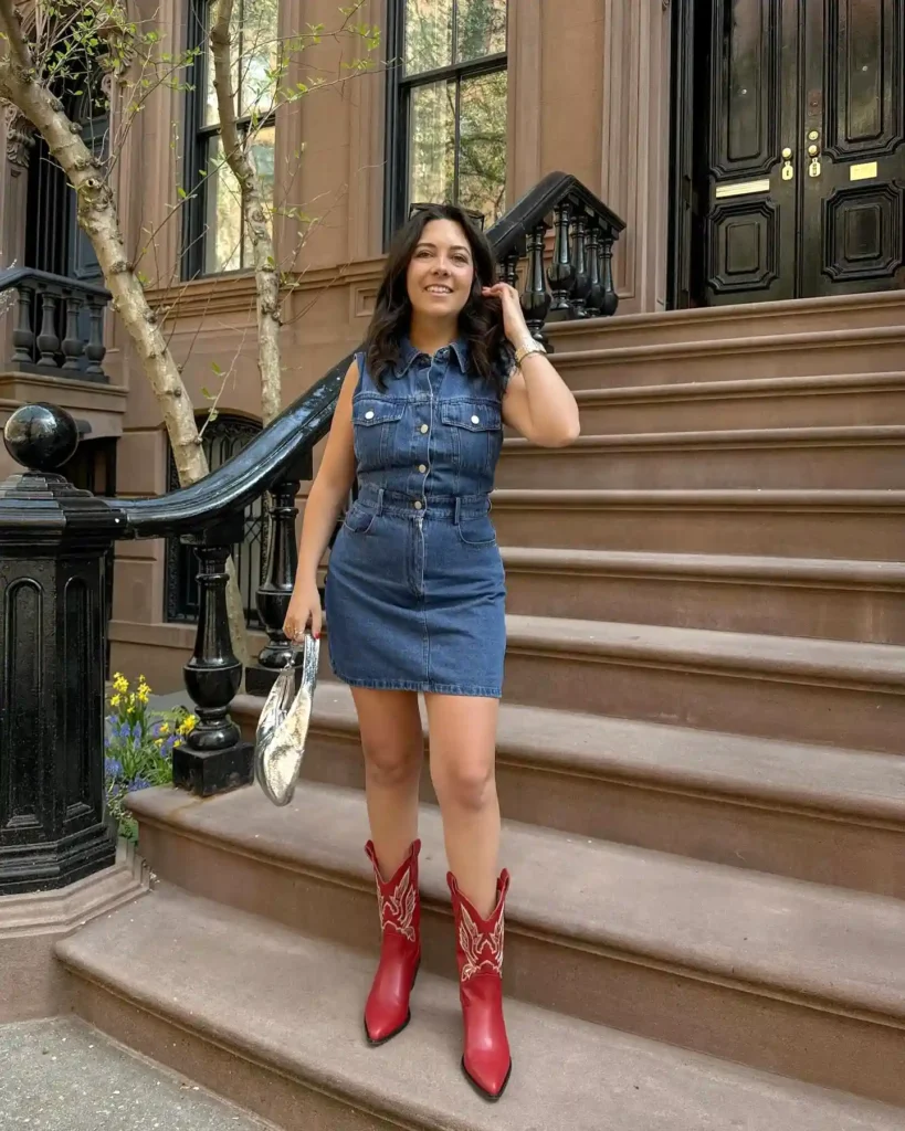 Woman in denim dress with red boots poses on urban steps, holding silver purse.