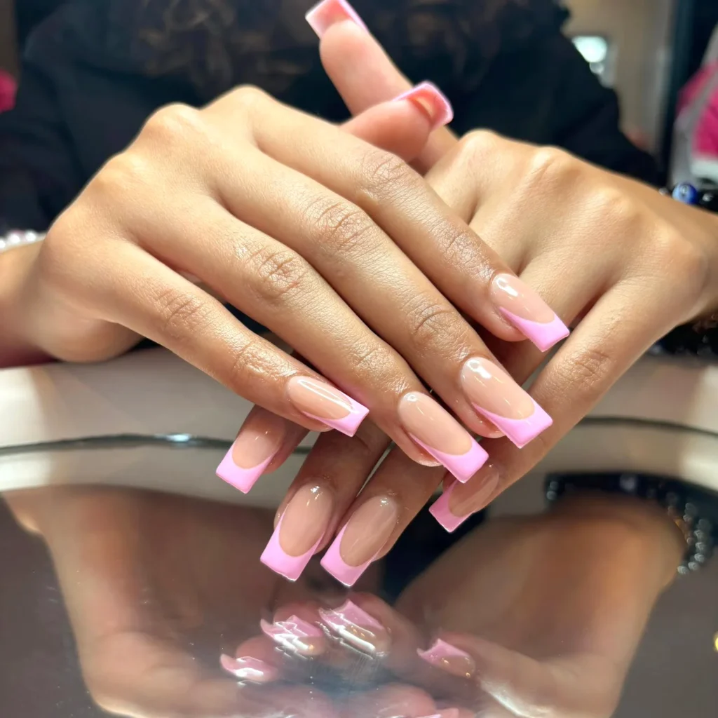 Pink French tips on manicured nails, elegantly styled hands resting on a reflective surface, showcasing nail art.