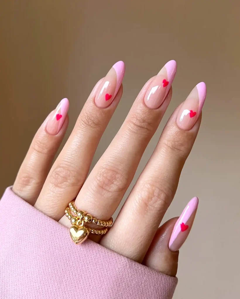 Pink manicure with heart details and gold rings on hand, elegant nail art design.