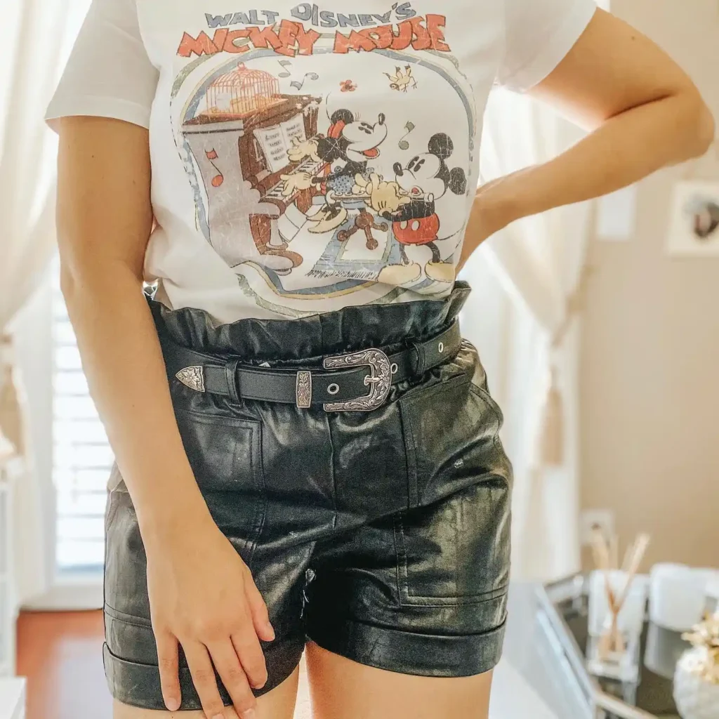 Person wearing a vintage Mickey Mouse t-shirt with high-waisted black leather shorts and a stylish belt.